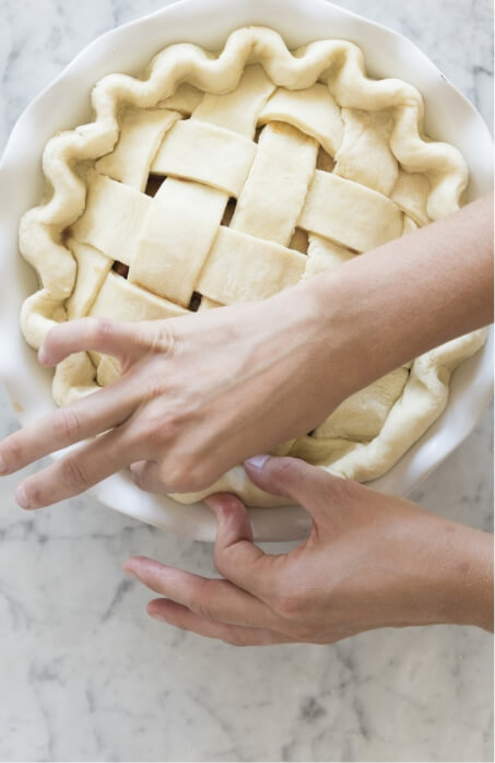 New Homes in a Family-Friendly Neighborhood showcase a person's hand putting a lattice on top of a pie.