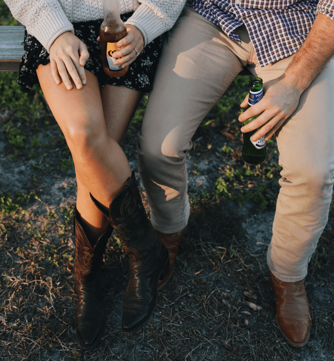 Two people sitting closely in one of the new home communities in Mansfield, TX, each holding a bottle, with a focus on their lower halves and autumnal attire.
