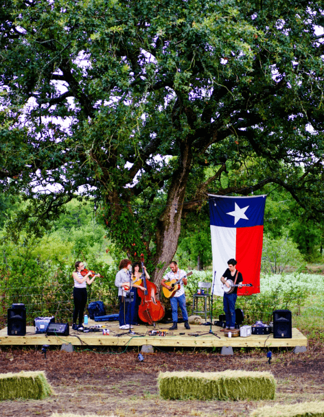 A band performing outdoors with a large Texas flag in the background near new homes in Goodland TX.