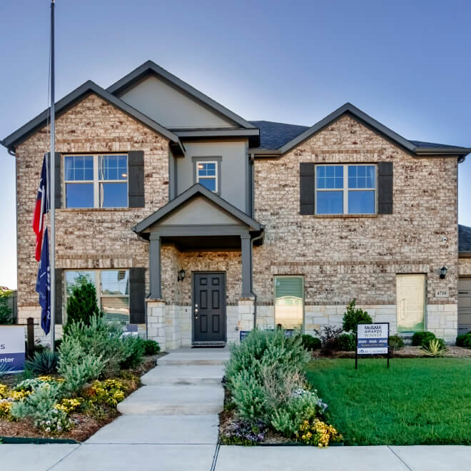 New two-story suburban house with a stone facade, landscaped garden, and American flag displayed outside in Goodland TX.