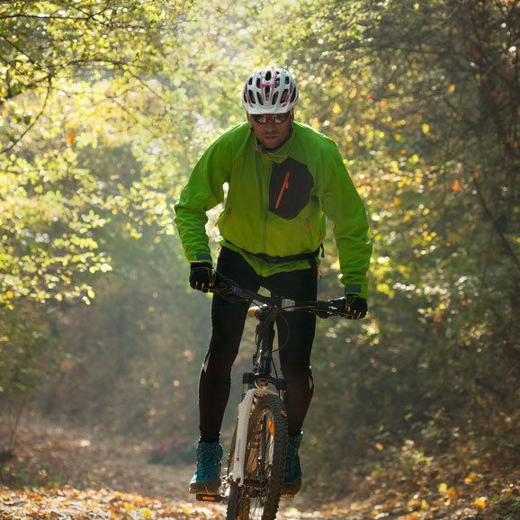 Cyclist in high-visibility jacket riding a mountain bike on a forest trail near new homes in Goodland TX.