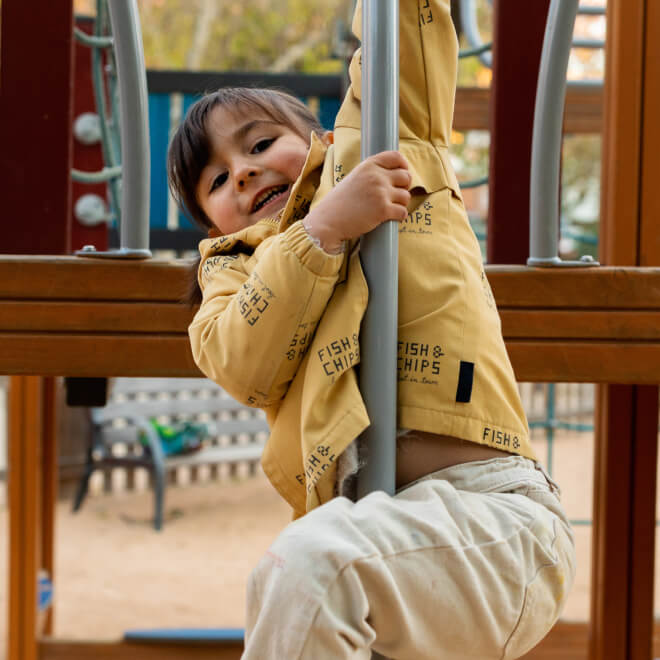 A smiling child clinging to a pole on a playground near new homes in Mansfield TX.