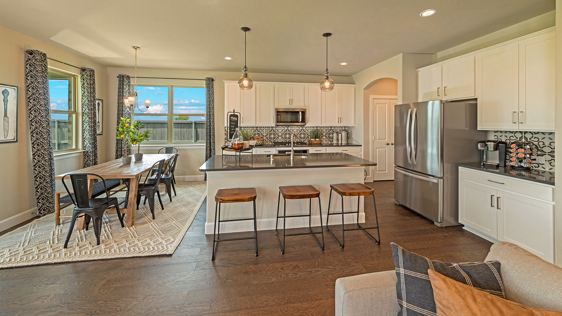 Modern kitchen and dining area in new home communities in Mansfield TX with stainless steel appliances, an island with bar stools, and a wooden dining table.