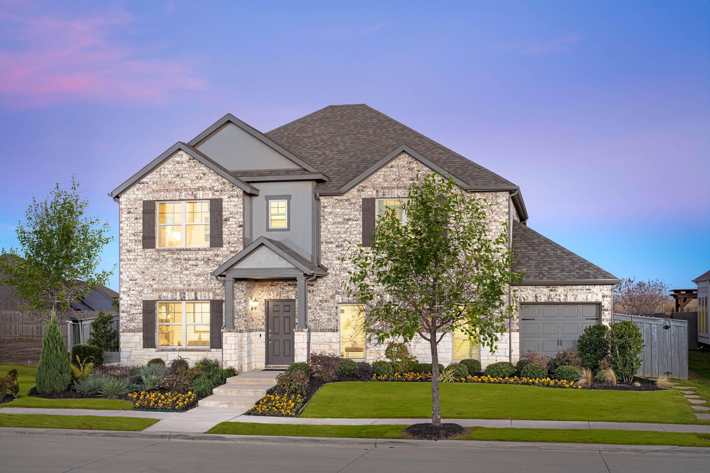 Two-story suburban home with stone facade at twilight in new home communities in Mansfield TX.