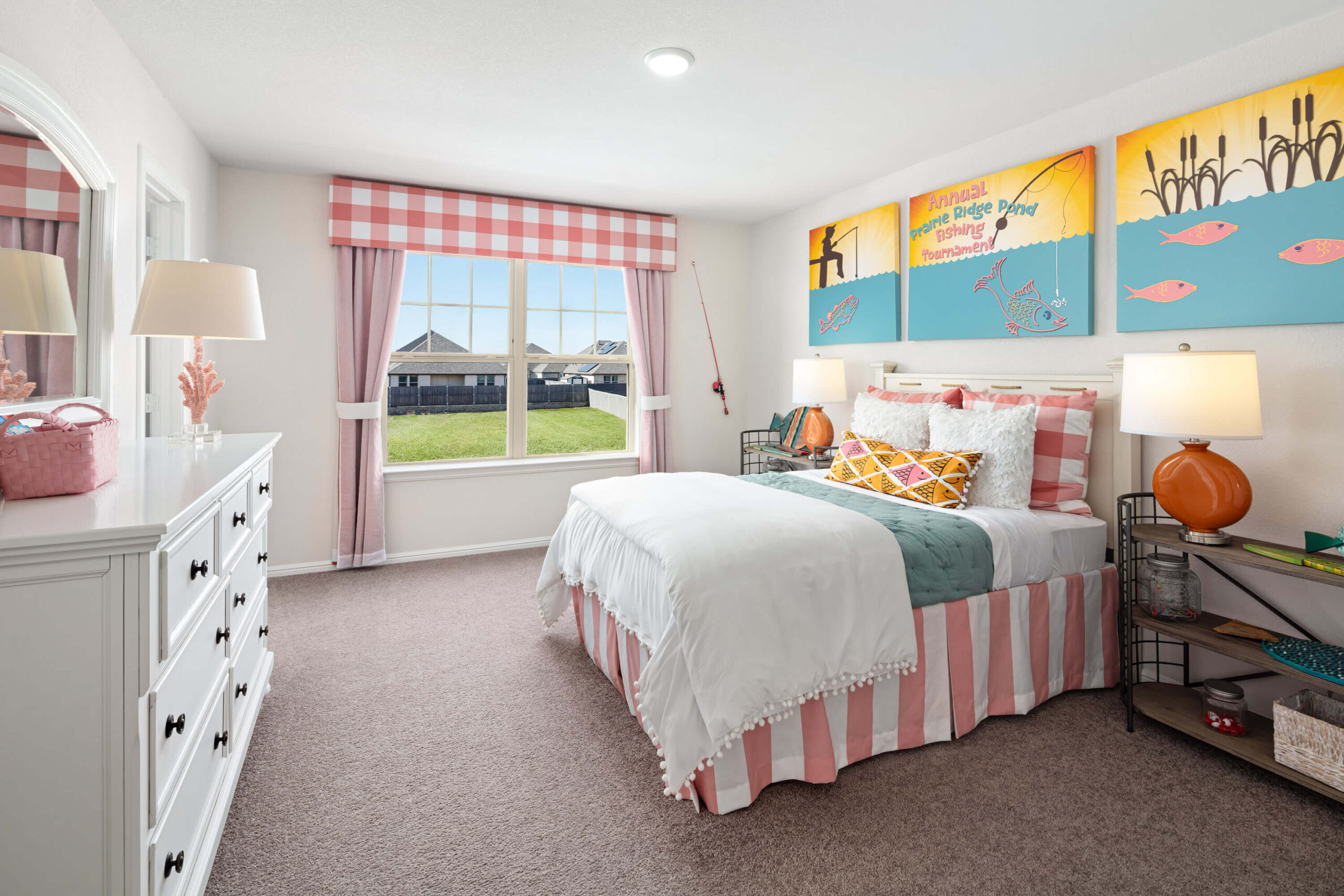 A brightly-lit, colorful bedroom in new homes in Mansfield TX, with a striped bedspread, decorative pillows, artwork on the wall, and a view of the outside through the window.