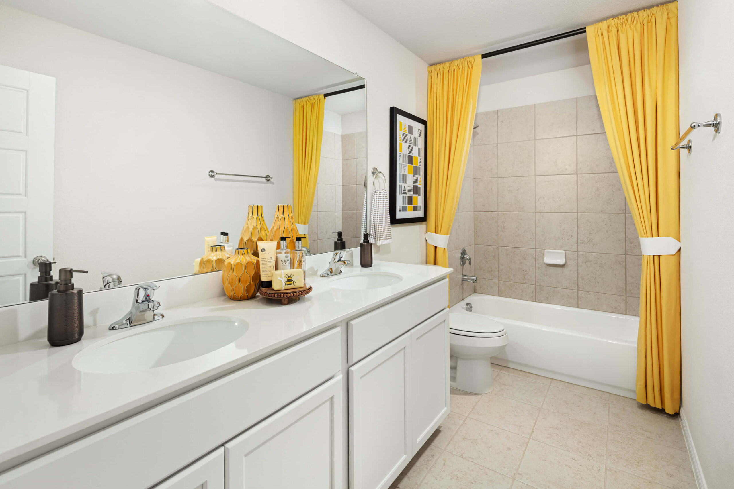 A clean, bright bathroom in new homes in Mansfield TX with a double vanity, a bathtub, and yellow accents.