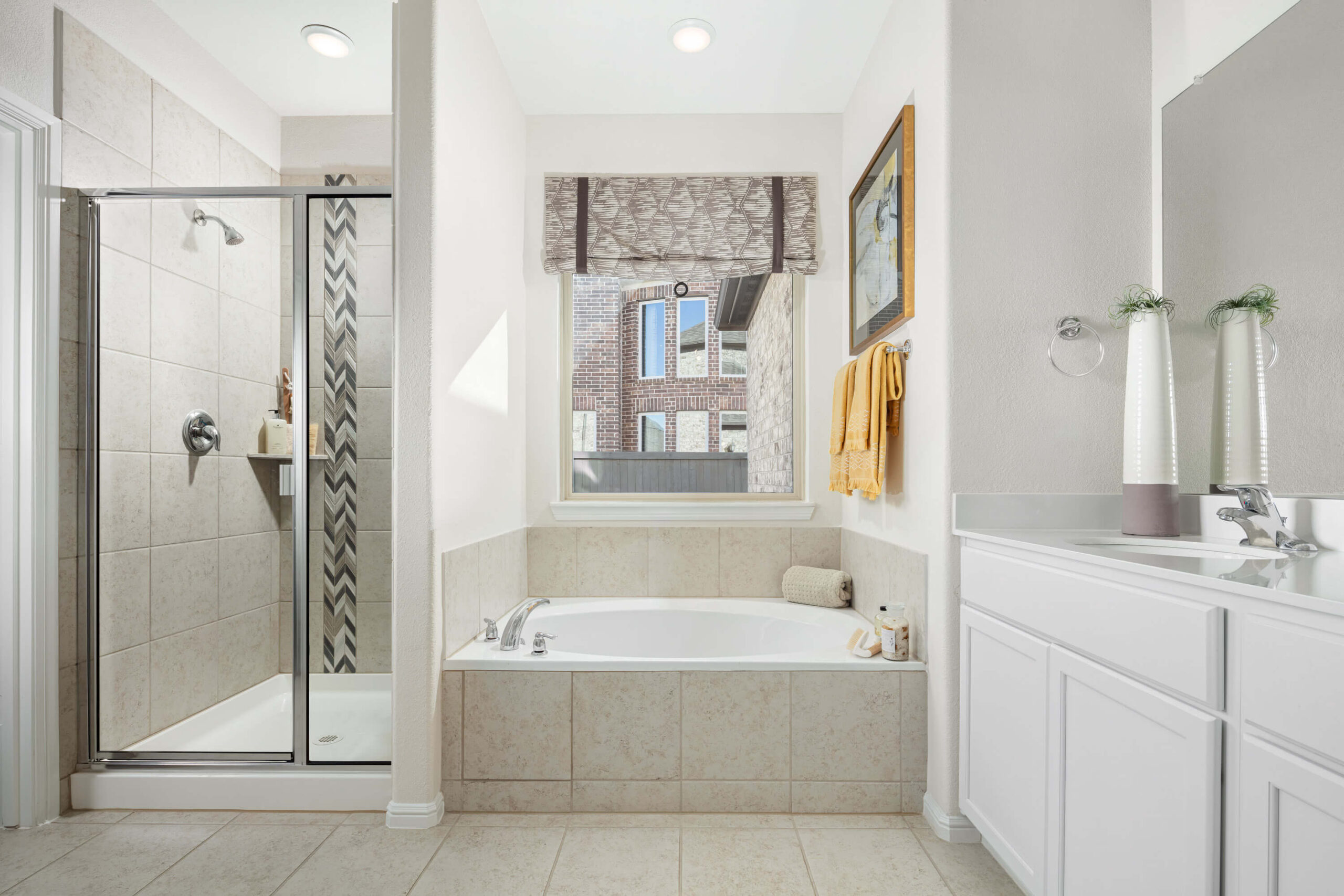 A well-lit, modern bathroom in new homes in Mansfield TX, featuring a shower stall, a bathtub, a vanity with a sink, and a window with a city view.
