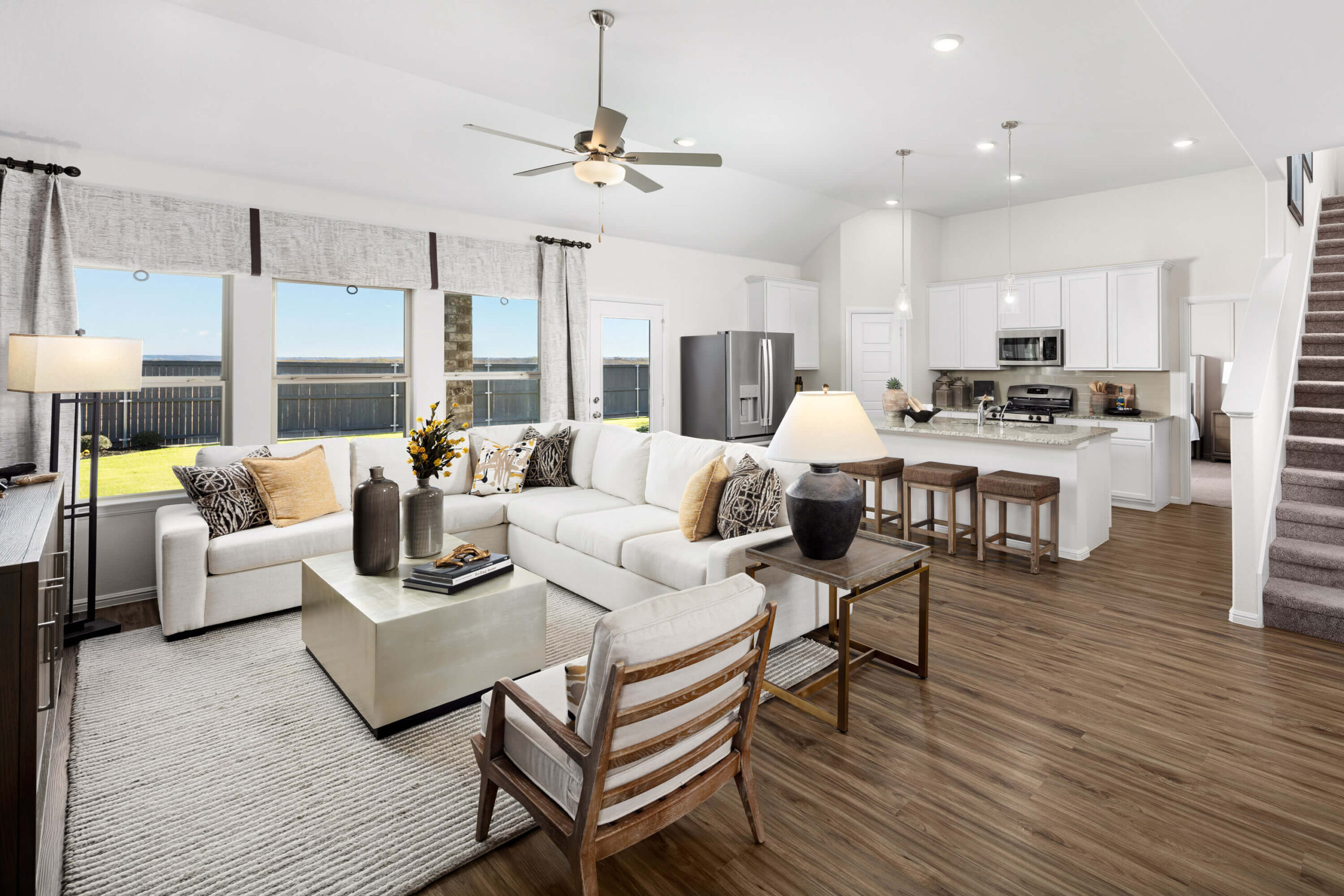 A bright, modern open-plan living room with a kitchen, dining, and lounge area in new homes in Mansfield TX, featuring contemporary decor and large windows.