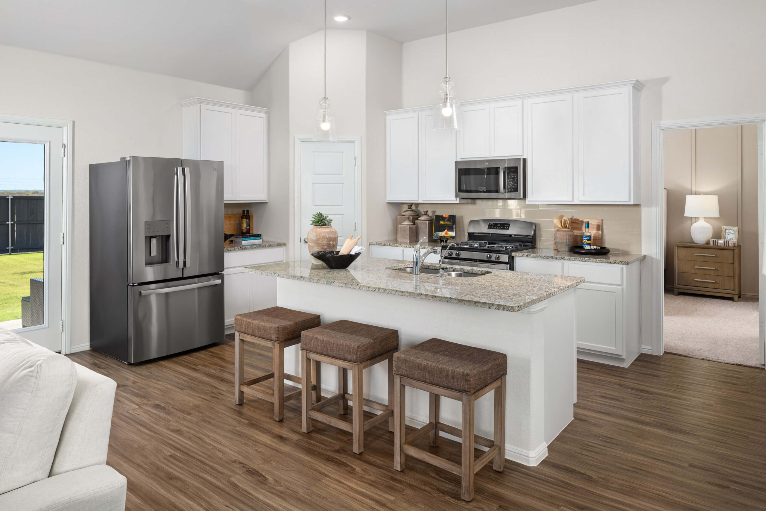 A modern kitchen interior in one of the new home communities in Mansfield TX, featuring white cabinetry, stainless steel appliances, and a central island with bar stools.