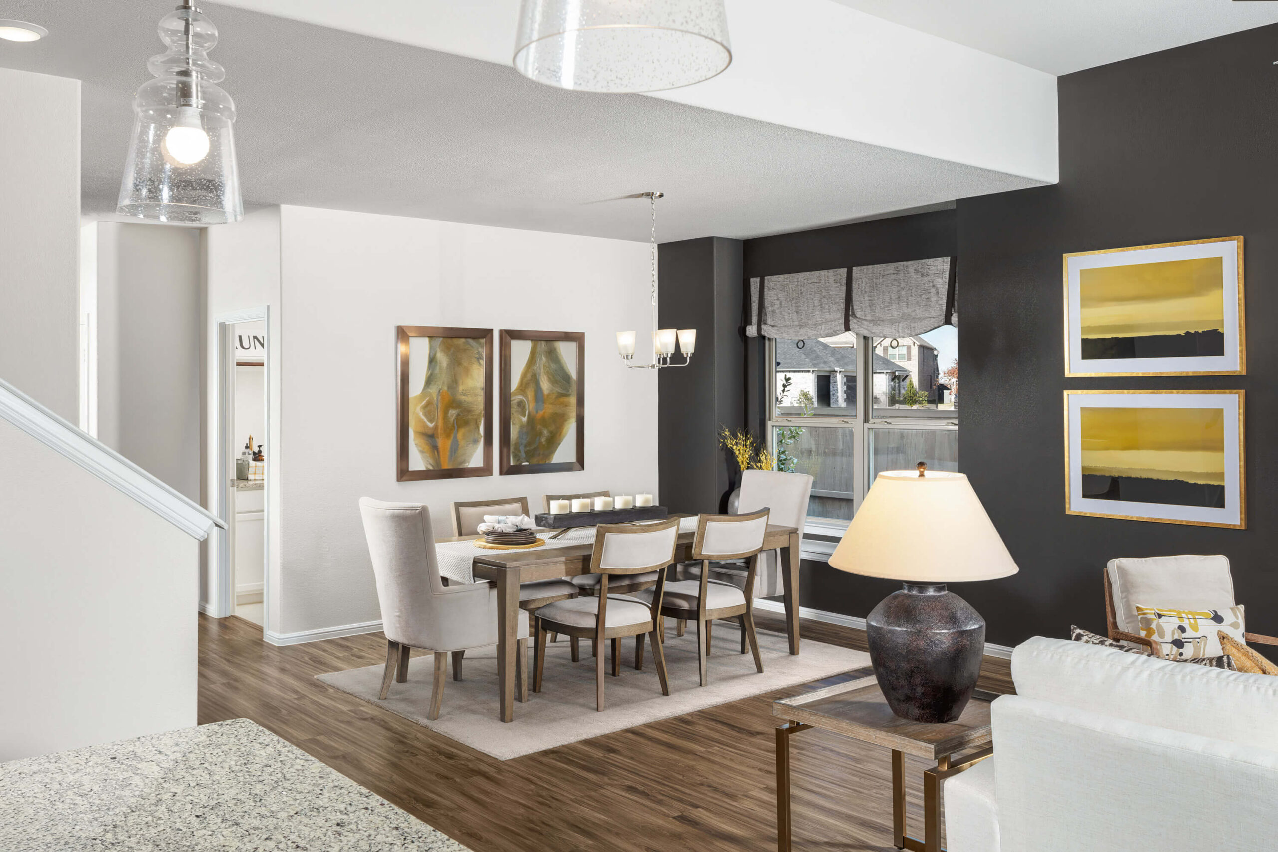 Modern dining room in new homes in DFW, featuring contrasting white and dark walls, a wooden table, upholstered chairs, and decorative artwork.