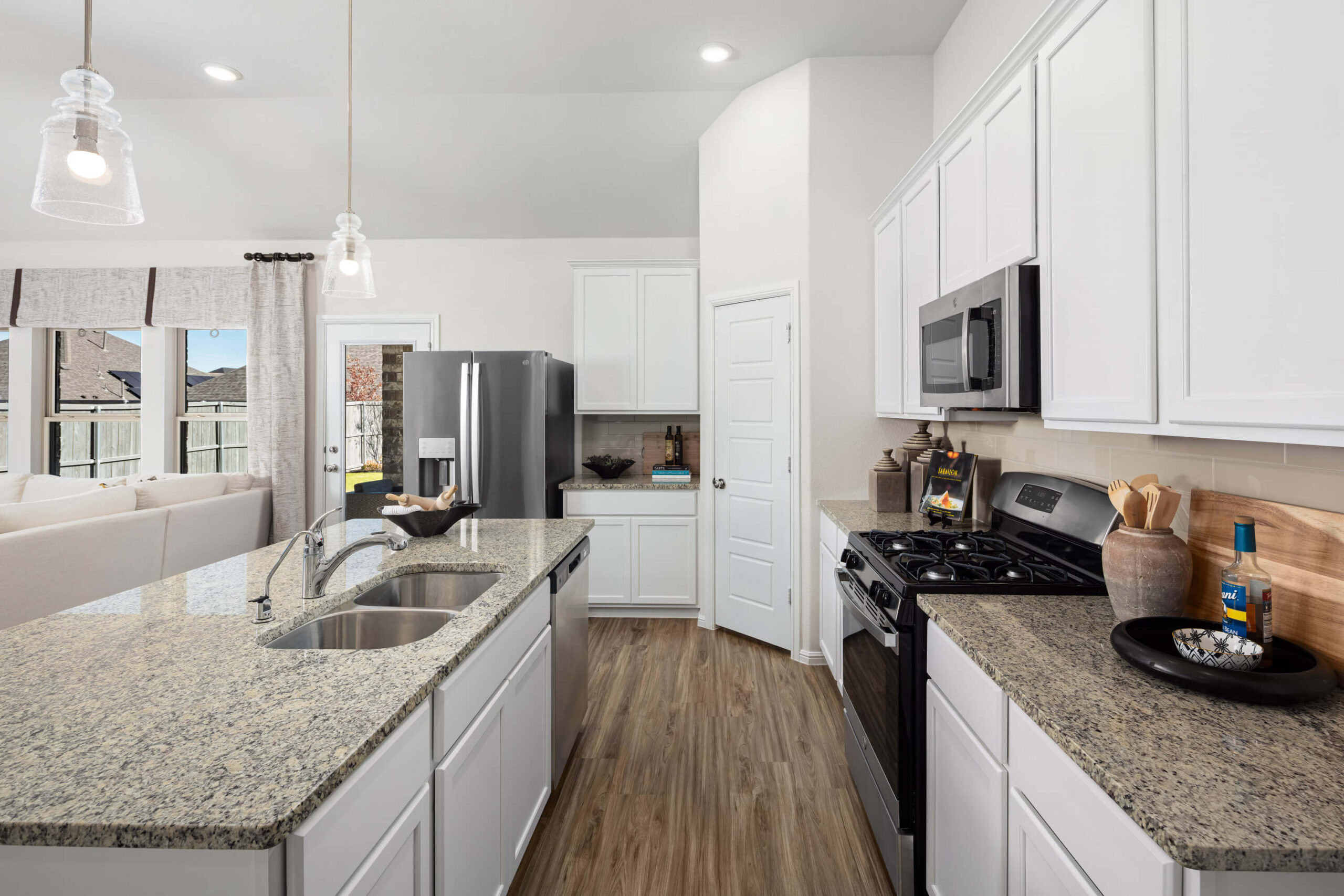 Modern kitchen interior with stainless steel appliances, white cabinetry, and granite countertops in new homes in DFW.