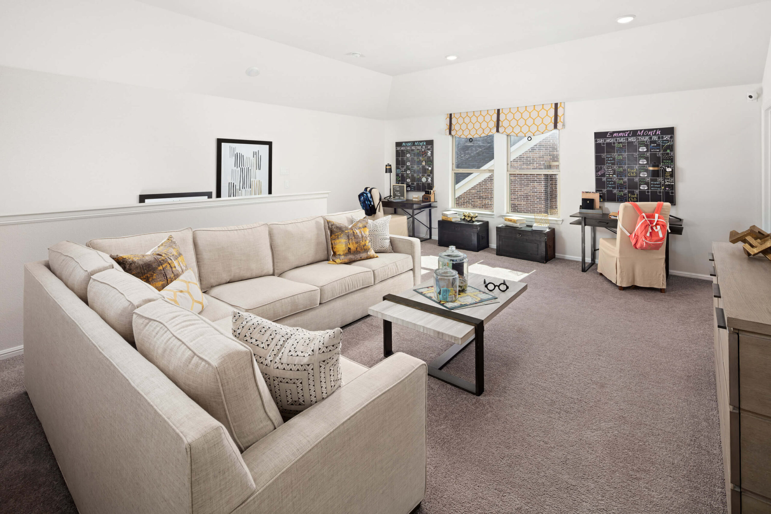 A spacious living room with a beige sectional sofa, patterned cushions, a glass coffee table, and a neatly organized entertainment area in new homes in Mansfield TX.