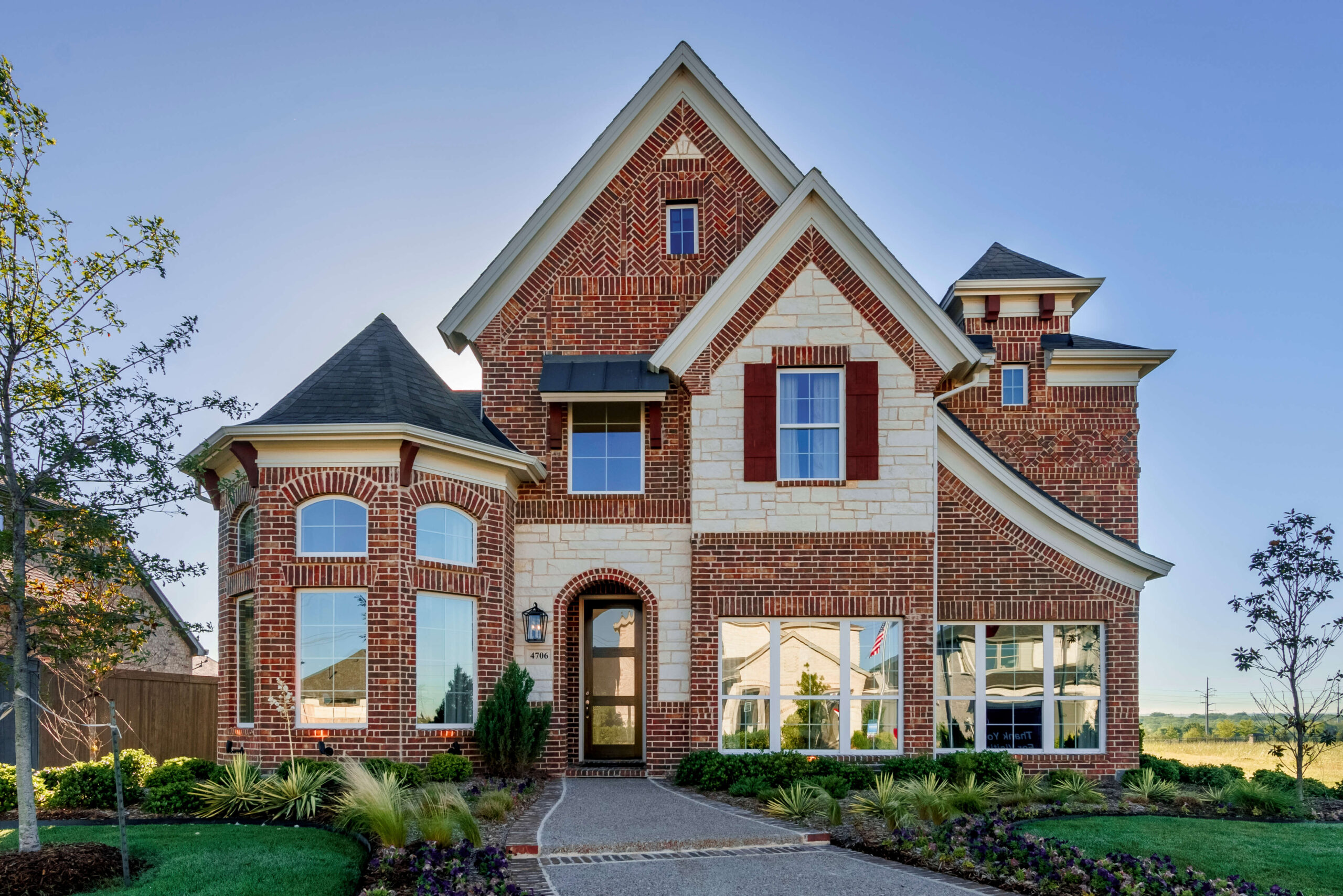 Two-story brick house with arched entryway and landscaped front yard in new home communities in Mansfield, TX.