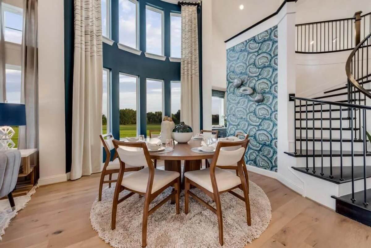 Modern dining room in new homes in Goodland TX with a wooden table, upholstered chairs, tall windows, and an adjacent spiral staircase.