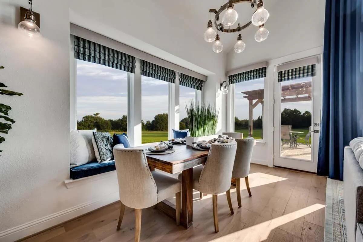 A bright and modern dining room in one of the new homes in Mansfield TX, with a wooden table, upholstered chairs, and a window bench overlooking a scenic outdoor view.