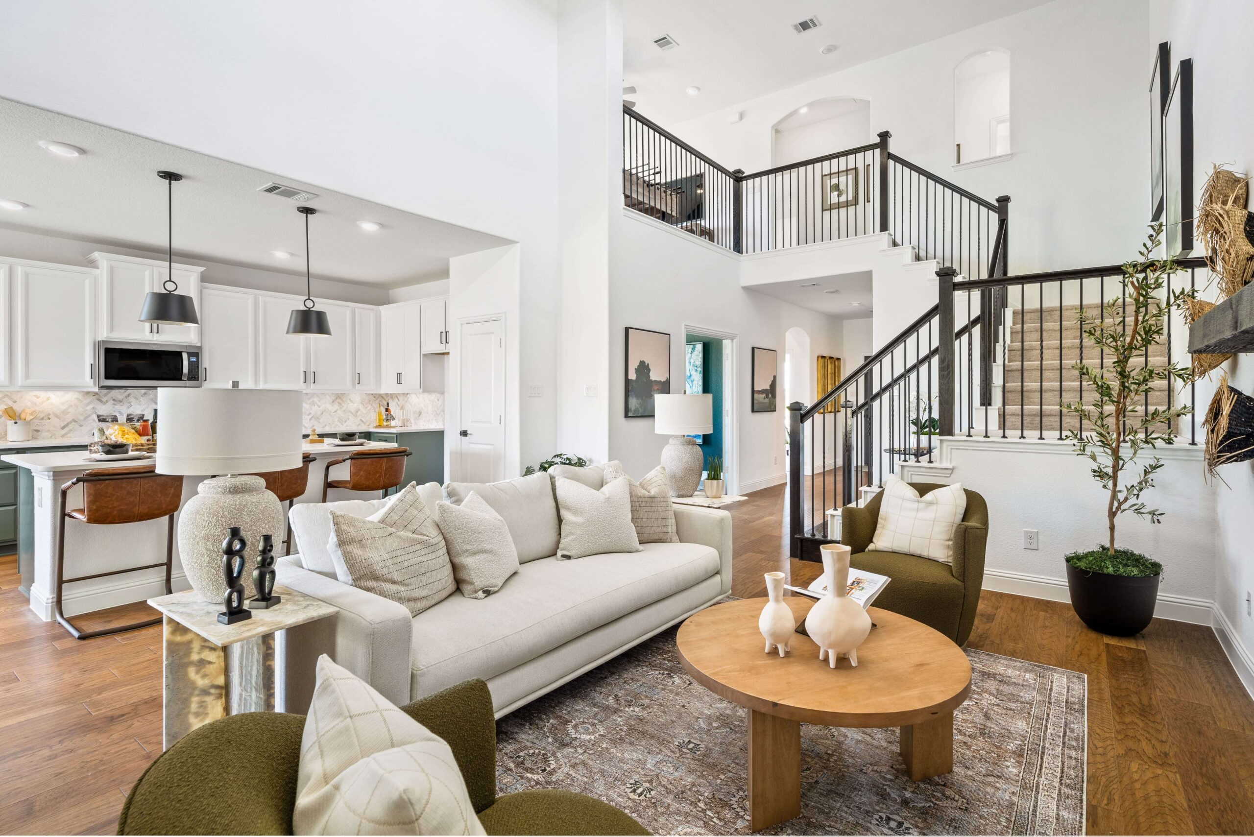 Open-concept living space in new homes in Goodland TX, featuring a living room with a beige sofa and accent chairs, and a kitchen with an island and modern appliances, complemented by bright,