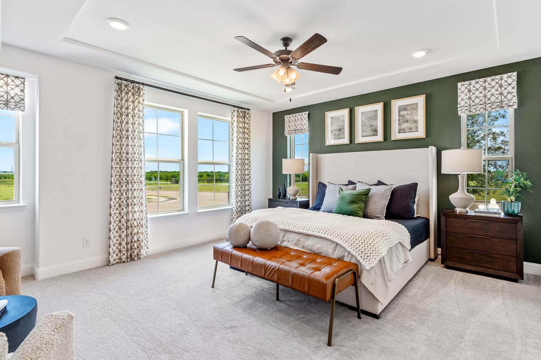 A modern bedroom in new homes in Mansfield TX with a green accent wall, white furnishings, and a ceiling fan.