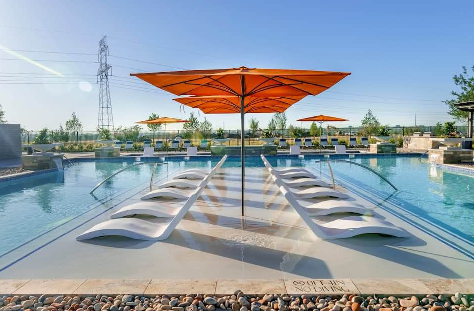 A serene outdoor pool area in one of the new home communities in Mansfield TX, featuring rows of sun loungers under large orange umbrellas on a sunny day.