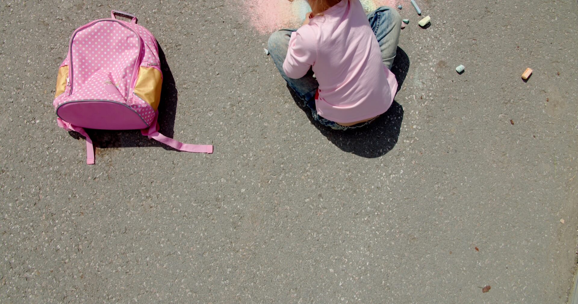 Child sitting on pavement in new home communities in Mansfield TX with a pink backpack and sidewalk chalk.
