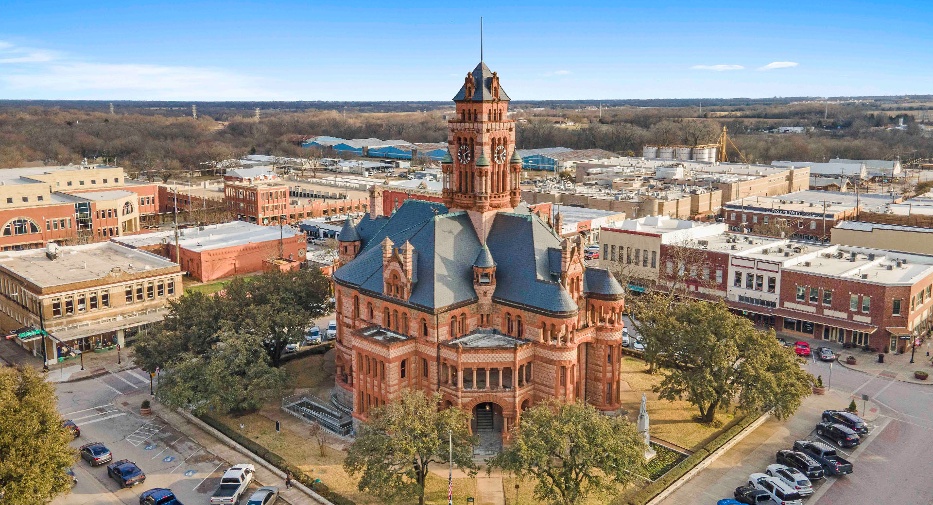 Aerial view of a historic red brick courthouse with a clock tower, surrounded by downtown buildings including new homes in Mansfield TX, in a small city.
