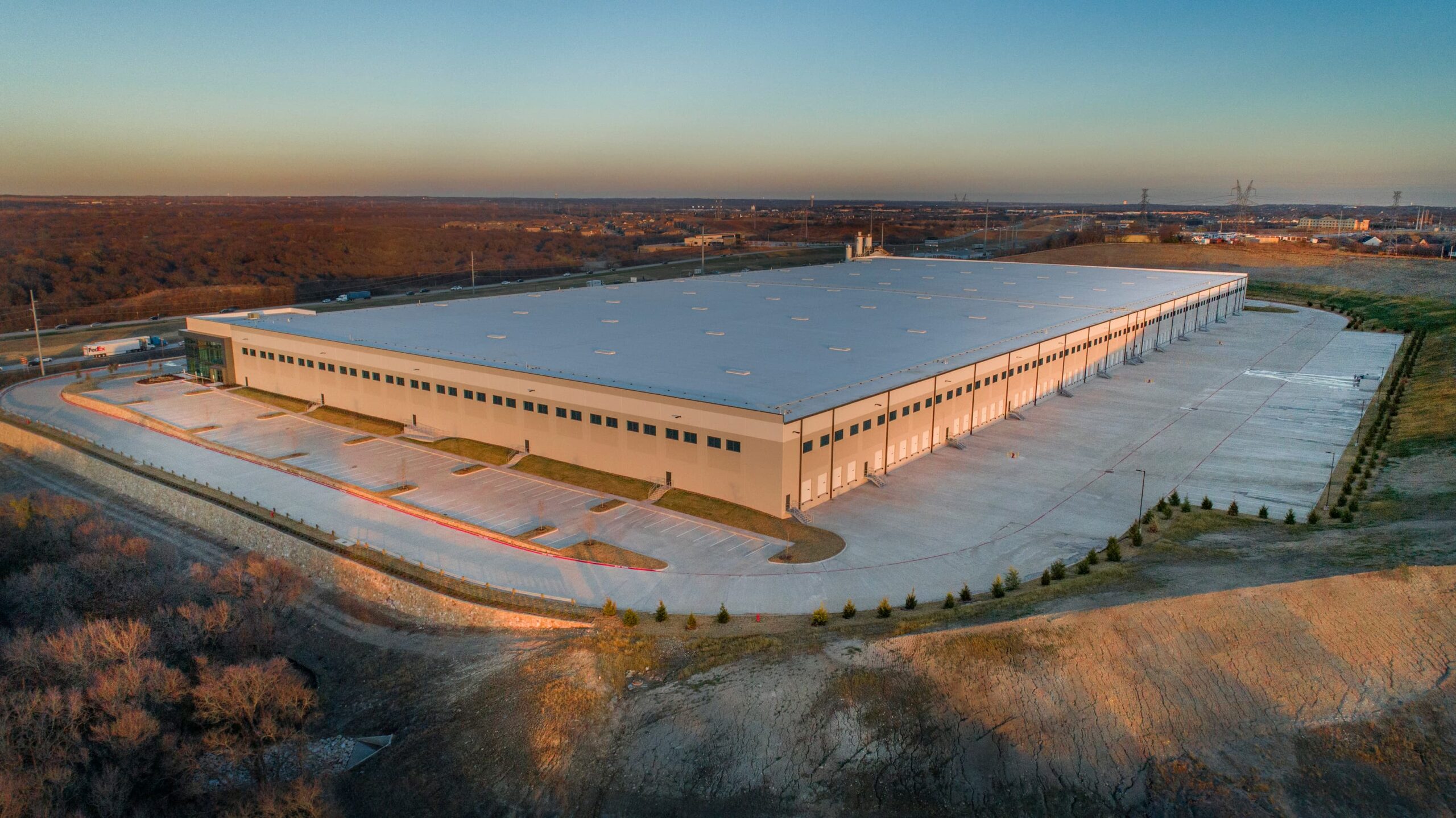 Aerial view of a large industrial warehouse at dusk with surrounding parking, access roads, and nearby new home communities in Mansfield TX.