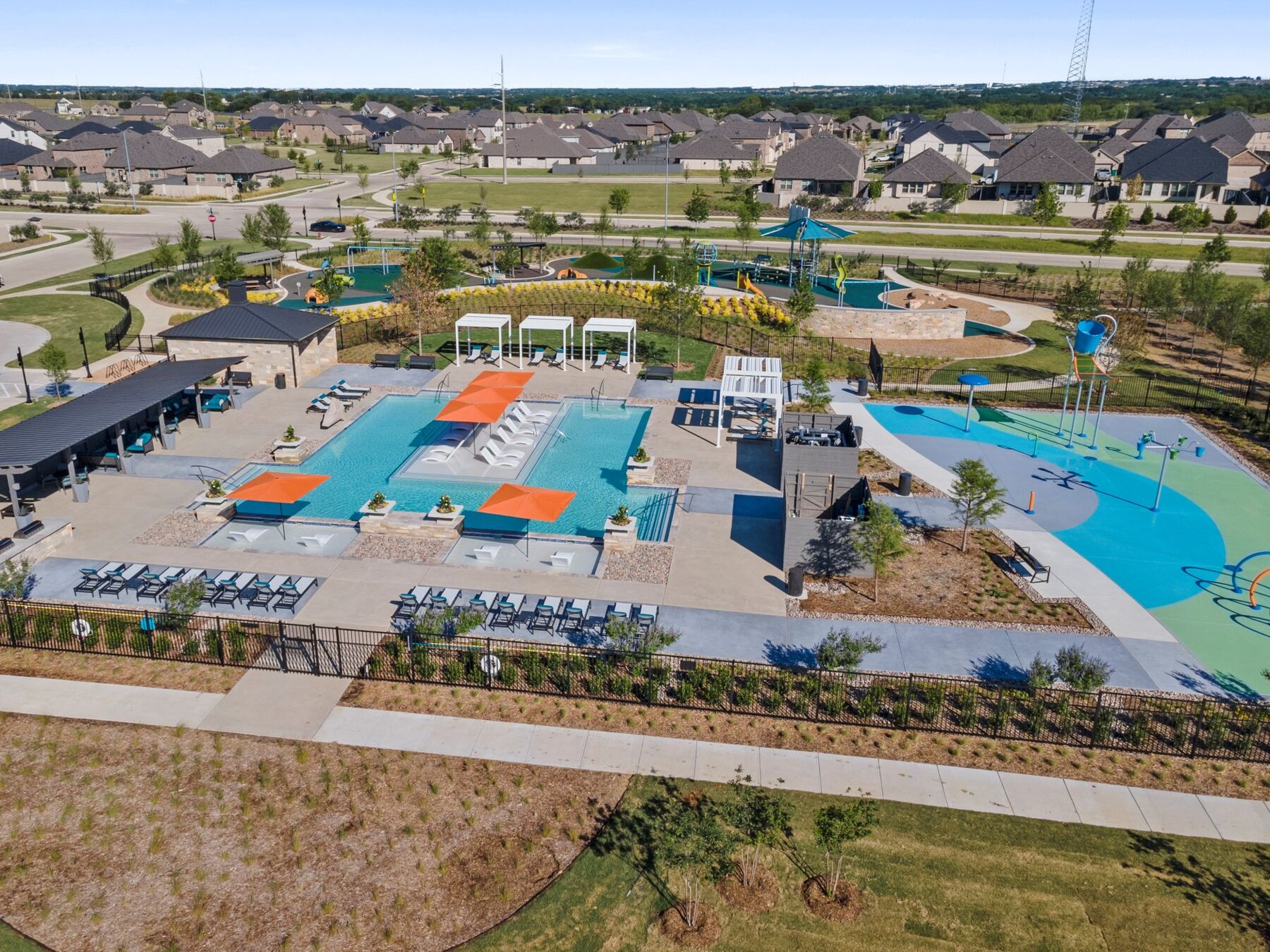 Aerial view of a suburban recreational area near new homes in Mansfield TX, featuring a swimming pool, lounge chairs, and a splash pad.