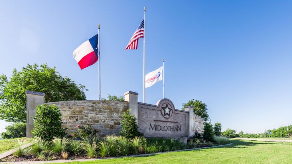 Flags of Texas, the United States, and the city of Midlothian flying at the entrance of Midlothian, Texas, near new homes in DFW.