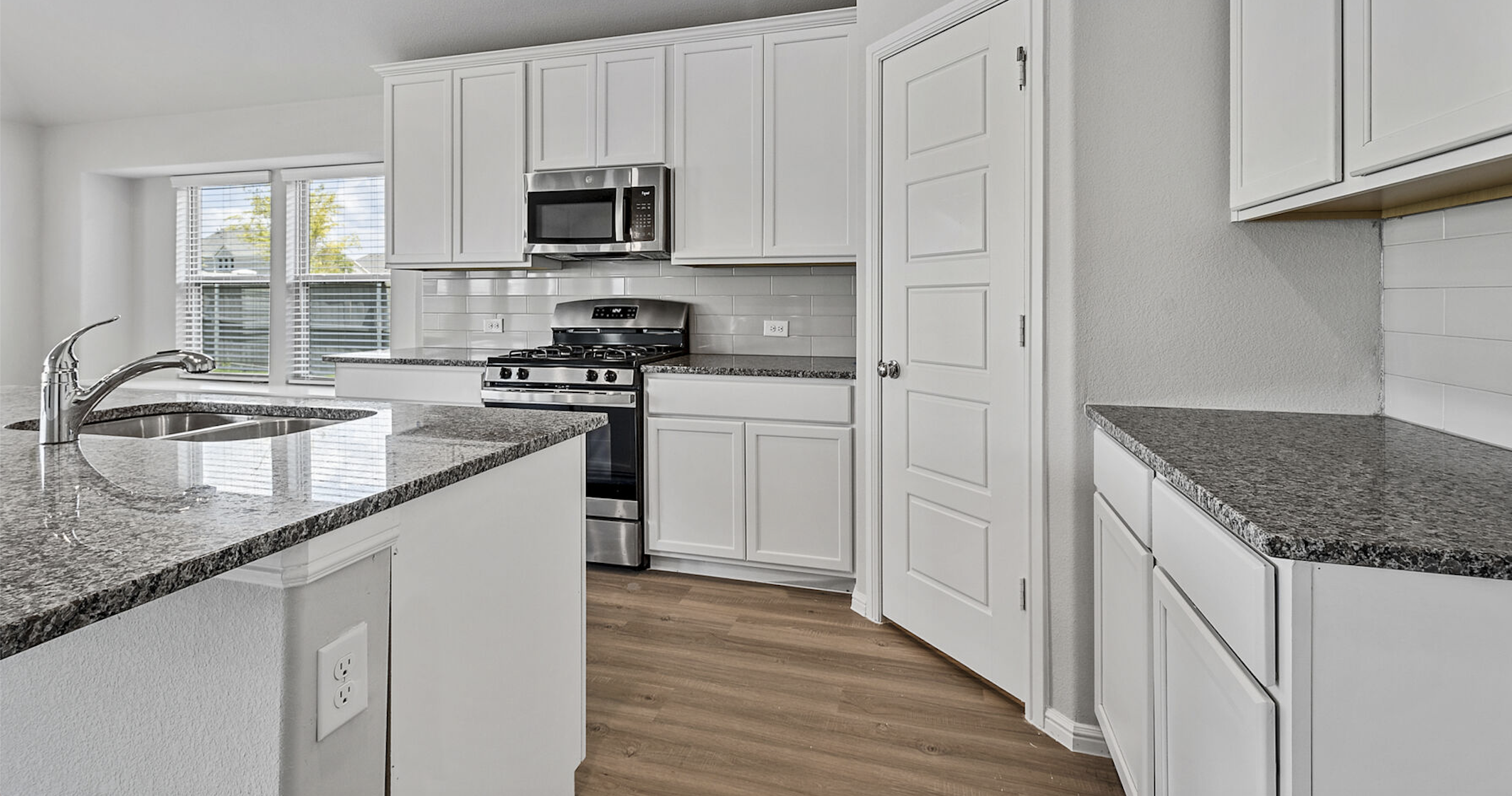 Modern kitchen in new homes in DFW with white cabinetry, stainless steel appliances, and granite countertops.