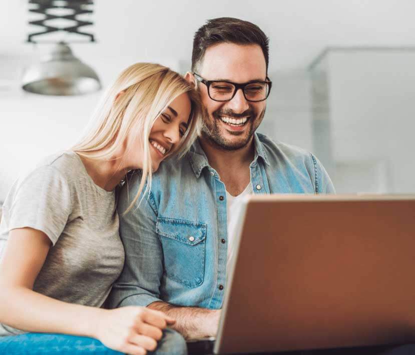 Two people smiling and looking at new homes in Mansfield TX on a laptop screen together.