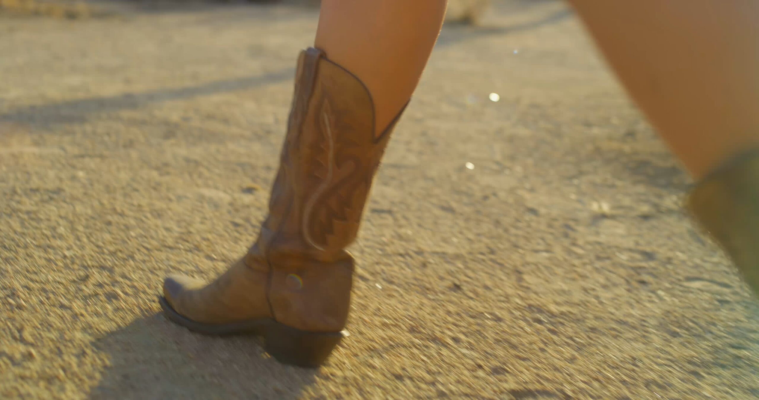 A person wearing a pair of brown cowboy boots on a sunlit, dusty ground, reminiscent of the atmosphere around new homes in Mansfield TX.