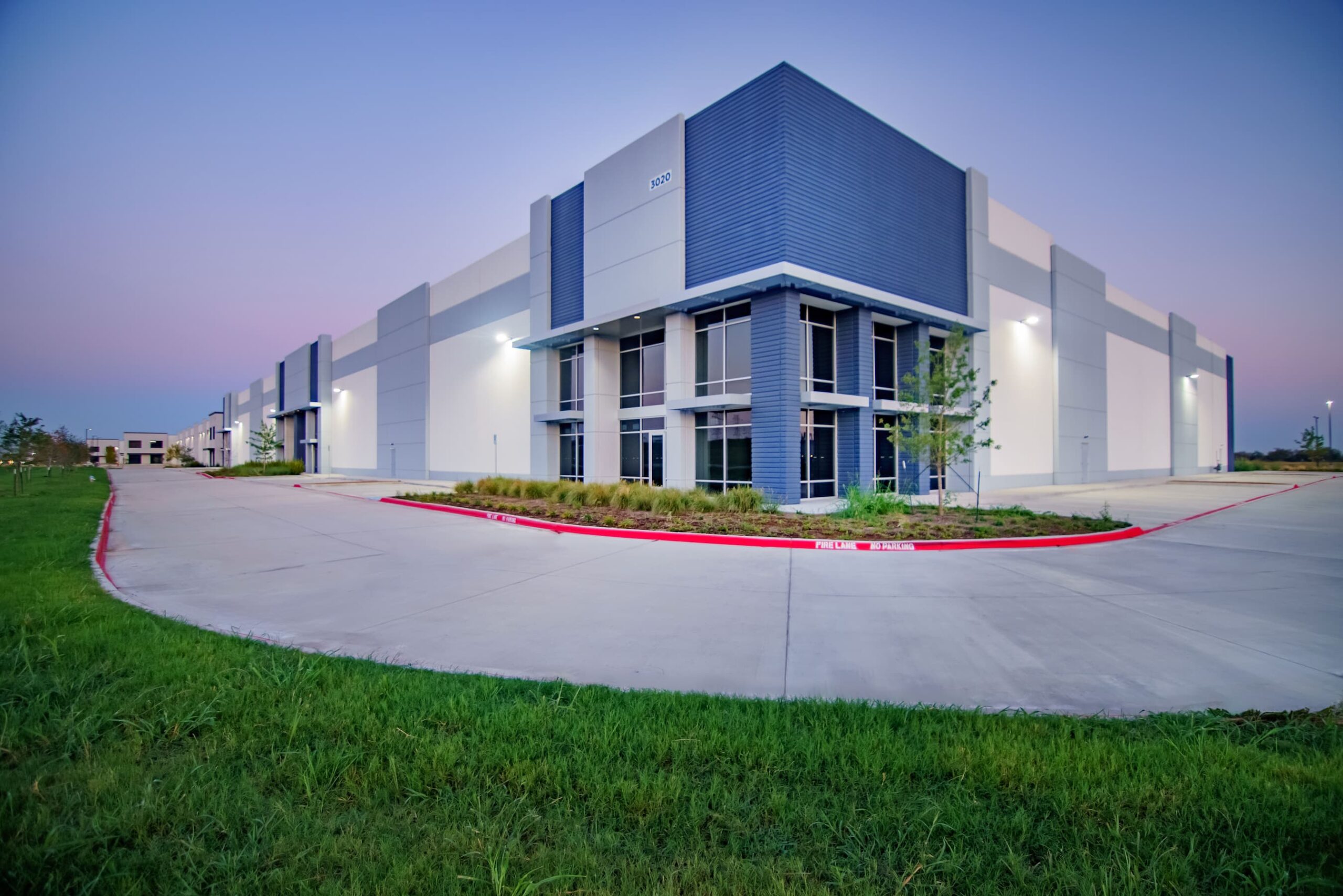 Modern industrial building exterior at twilight with landscaped frontage near new homes in Mansfield TX.