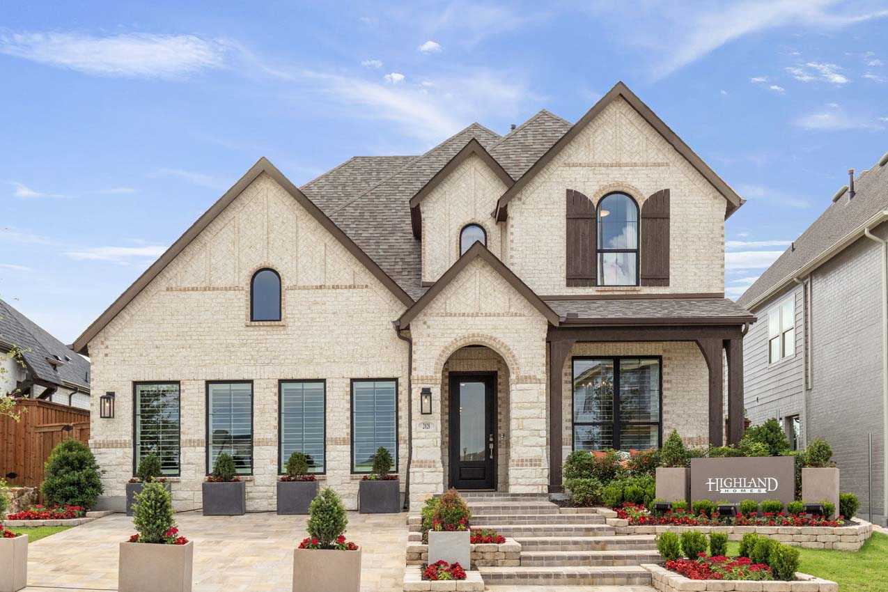 Two-story modern suburban house with light brick exterior, dark shutters, landscaped front yard, and a sign reading "Highland Homes.