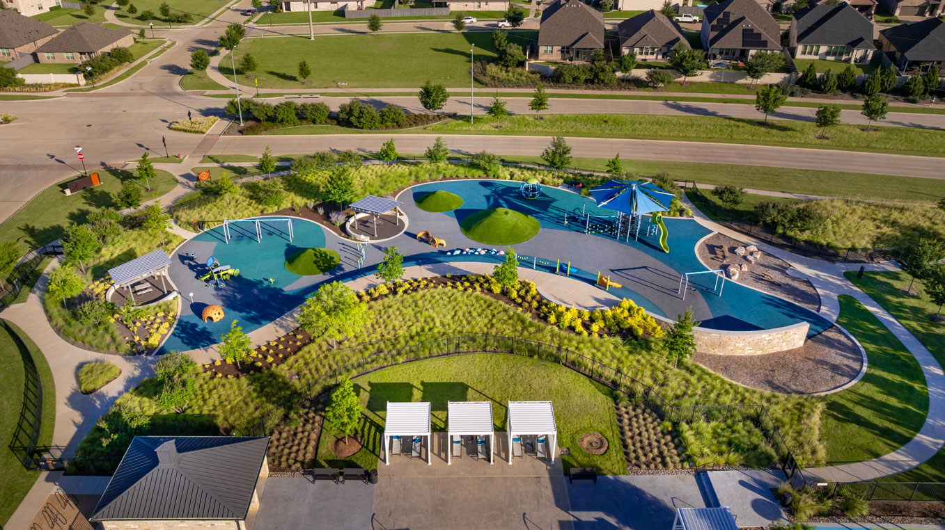 Aerial view of a modern playground with play structures, swings, climbing areas, slides, shaded seating, and landscaped greenery in one of the vibrant communities with pools near me.
