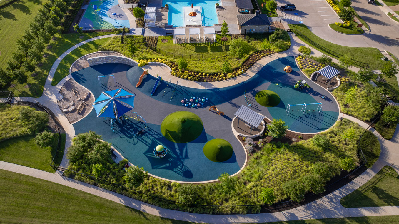 Aerial view of a modern playground with climbing structures, slides, swings, and shaded seating areas, nestled in lush green lawns and walking paths—perfect for families seeking communities with pools near me.