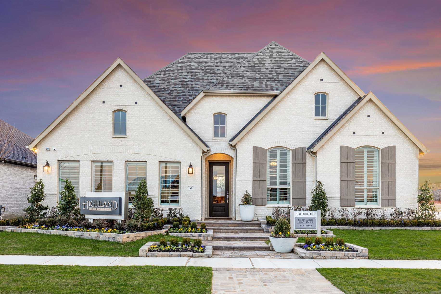 Two-story modern house with light brick exterior, gabled roof, large windows, and a landscaped yard—an inviting example of new homes in Mansfield TX—features “Highland Homes” and “Sales Office” signs near the entrance.