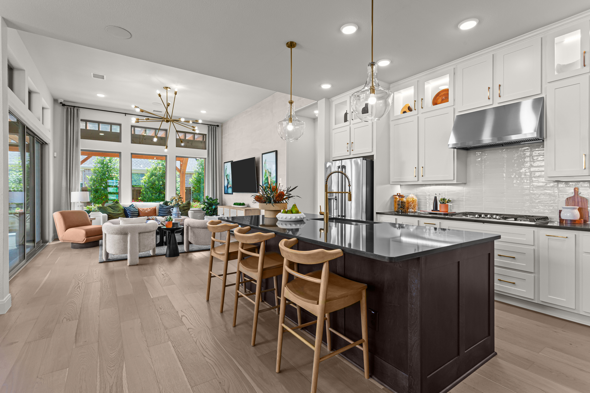 Modern open-concept kitchen and living area, inspired by model homes Dallas, with a dark island, light wood floors, white cabinets, and large windows letting in natural light.